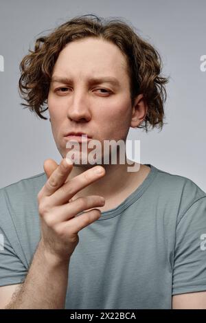 Vertikales mittleres Nahaufnahme-Studio-Porträt eines skeptischen jungen kaukasischen Mannes, der für die Kamera posiert, grauer Hintergrund Stockfoto