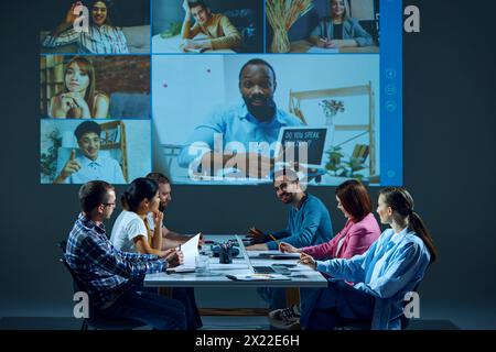 Mitarbeiter, die im Sitzungssaal sitzen, nehmen an virtuellen Besprechungen mit Kollegen an entfernten Standorten per Online-Videoanruf Teil Stockfoto