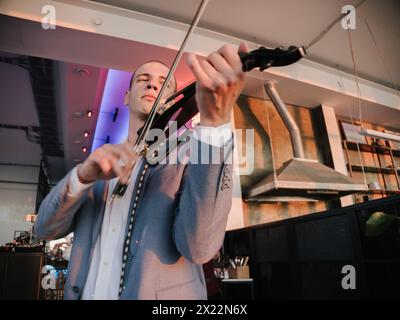 Der Geiger setzt sich mit elektrischer Violine, Leidenschaft in seinem Ausdruck, in lebendiger Beleuchtung ein. Stockfoto