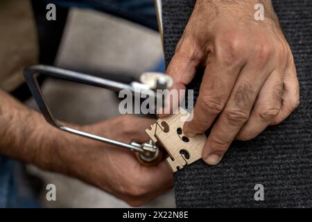 Blick von oben auf einen nicht erkennbaren lateinamerikanischen Geigenbauer mit einer Bügelsäge, um eine Geigenbrücke zu fertigen. Das Konzept der Streichinstrumente Stockfoto