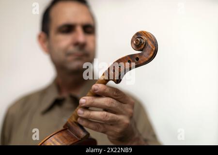 Lateinamerikanischer Geigenbauer hält eine unvollendete Violine in den Händen, wobei er selektiv auf die Violine fokussiert. Konzeptinstrumente Stockfoto