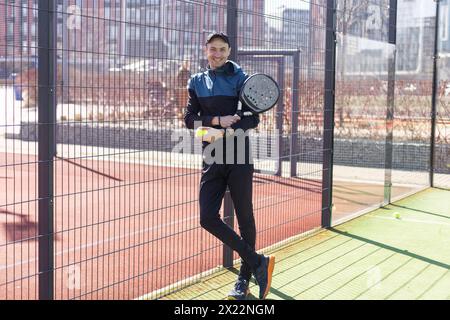 Porträt eines positiven jungen Mannes mit Schläger und Padel-Ball auf dem Tennisplatz Stockfoto