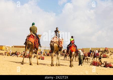 Gruppe von Touristen auf einem Kamelritt der Beduinen Rückkehr zum Kamelpark, an den Großen Pyramiden von Gizeh, Kairo, Ägypten Stockfoto