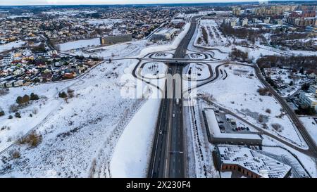 Drohnenfotografie einer hochintensiven Straße in der Nähe von Stadträndern, umgeben von Gebäuden am sonnigen Wintermorgen Stockfoto