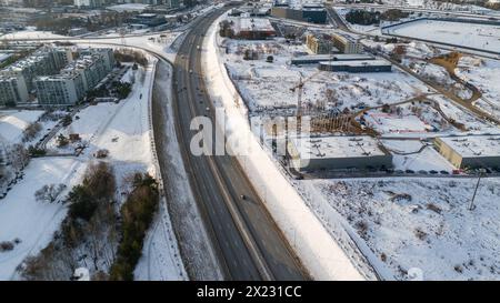 Drohnenfotografie einer hochintensiven Straße in der Nähe von Stadträndern, umgeben von Gebäuden am sonnigen Wintermorgen Stockfoto