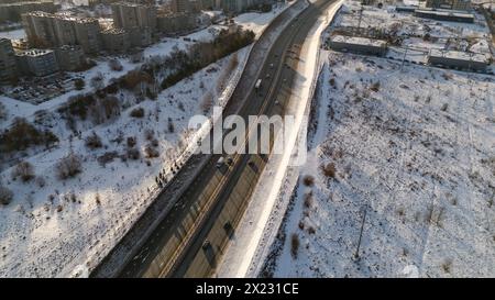 Drohnenfotografie einer hochintensiven Straße in der Nähe von Stadträndern, umgeben von Gebäuden am sonnigen Wintermorgen Stockfoto