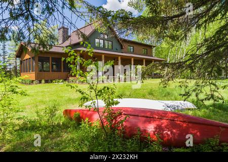 Rückansicht von braun und grün gebeiztem Fichtenholz und Zedernschindel, das LEED-zertifiziertes Landhaus mit Veranda im späten Frühjahr in Quebec, Kanada Stockfoto