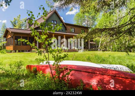 Rückansicht von braun und grün gebeiztem Fichtenholz und Zedernschindel, das LEED-zertifiziertes Landhaus mit Veranda im späten Frühjahr in Quebec, Kanada Stockfoto