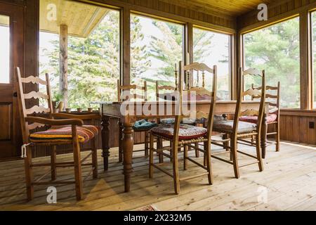 Sonnenzimmer mit antikem Esstisch aus Holz und Stühlen, behandelten Holzdielen in einem LEED-zertifizierten Landhaus in Quebec, Kanada Stockfoto