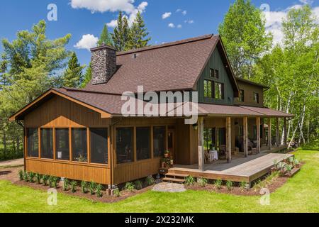 Erhöhte Rückansicht von braun und grün gebeiztem Fichtenholz und Zedernschindel, die als LEED-zertifiziertes Landhaus mit Veranda im späten Frühjahr, Quebec, dienen Stockfoto