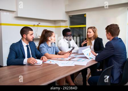 Weibliche Führungskraft leitet globale Geschäftsaufträge mit multikulturellen Teams in modernen Büros und diskutiert Diagramme. Verschiedene Gruppen von Fachleuten engagieren sich Stockfoto