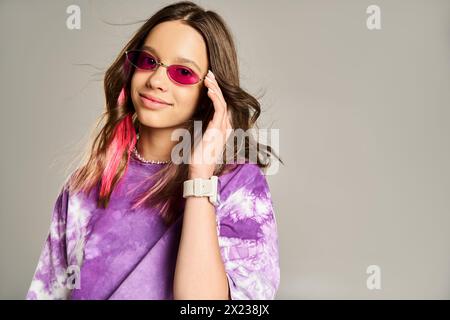 Stilvolles Teenager-Mädchen posiert selbstbewusst in rosa Haaren und lila Hemd und trägt eine trendige Sonnenbrille. Stockfoto