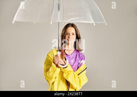 Ein modisches Teenager-Mädchen, das einen leuchtend gelben Regenmantel trägt, posiert an einem regnerischen Tag mit einem Regenschirm. Stockfoto