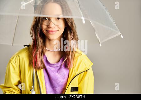 Ein stilvolles Mädchen im Teenageralter in lebendiger Kleidung hält einen klaren Regenschirm in aktiver Pose über dem Kopf. Stockfoto