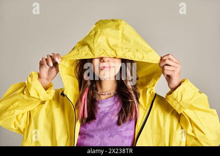 Ein Teenager in einem gelben Regenmantel, der ihr Gesicht mit den Händen in einer lebhaften Pose bedeckt. Stockfoto