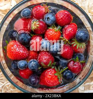 Das Ober-Bild gewaschener Erdbeeren und Heidelbeeren im Wasser in einer Glasschale Stockfoto