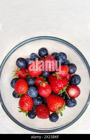 Überkopfbild gewaschener Erdbeeren und Heidelbeeren in Glasschale auf Holztisch Stockfoto