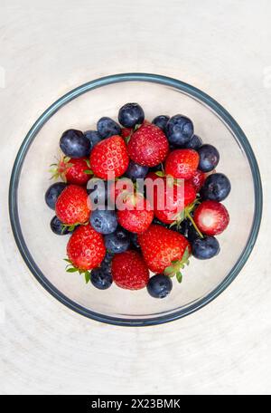 Überkopfbild gewaschener Erdbeeren und Heidelbeeren in Glasschale auf Holztisch Stockfoto