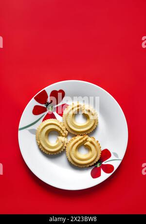 Wiener Vanillebrötchen auf weißem Teller mit rotem Blumenmuster auf rotem Hintergrund Stockfoto