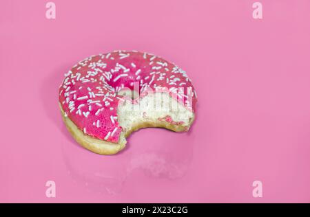 Rosa Eisring Donut mit Streuseln, herausgenommen, auf rosafarbenem Hintergrund und partieller Reflexion Stockfoto
