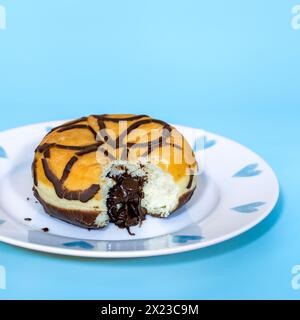 Mit Schokolade gefüllter Donut mit herausgenommenem Biss, und sprudelnder Schokoladenfüllung, auf blauem Hintergrund und hübschem Teller Stockfoto