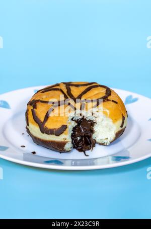 Mit Schokolade gefüllter Donut mit herausgenommenem Biss, und sprudelnder Schokoladenfüllung, auf blauem Hintergrund und hübschem Teller Stockfoto