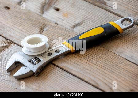 Verschiedene Sanitär-Ersatzteile, weißes Dichtband und verstellbarer Schraubenschlüssel auf Holzhintergrund. Nahaufnahme Stockfoto