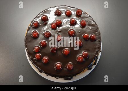 Weißer Biskuitkuchen „Drunken Cherry“, dekoriert mit Schokoladenglasur mit karamellisierten, roten und hellen, süßen Kirschen. Stockfoto