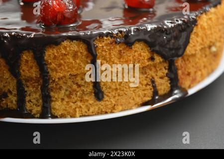 Weißer Biskuitkuchen „Drunken Cherry“, dekoriert mit Schokoladenglasur mit karamellisierten, roten und hellen, süßen Kirschen. Stockfoto