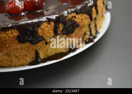Weißer Biskuitkuchen „Drunken Cherry“, dekoriert mit Schokoladenglasur mit karamellisierten, roten und hellen, süßen Kirschen. Stockfoto