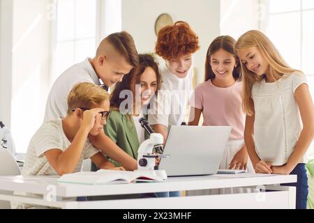 Gruppe von Schülern, die mit dem Lehrer im Klassenzimmer sitzen und während des Unterrichts auf den Laptop schauen. Stockfoto
