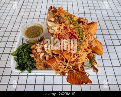 Plaa Tod Samoon Prai ist ein thailändisches Gericht mit frittiertem Fisch und einem Kräutersalat, serviert mit Naam jim, einer scharfen Chili-Sauce. Stockfoto