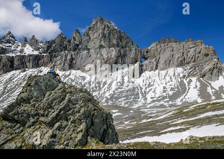 Mann und Frau wandern auf einem Felsen sitzen und auf Tschingelhörner mit Martinsloch, Plaun Segnas Sut, Unterer Segnesboden, Sardona Tectonic Arena schauen Stockfoto