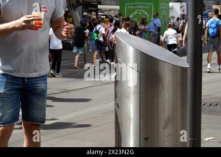 Ein Mann warf etwas in einen Street Metal Mülleimer. Seine Hand ist unfokussiert, weil sie sich noch in Bewegung befindet. Stockfoto