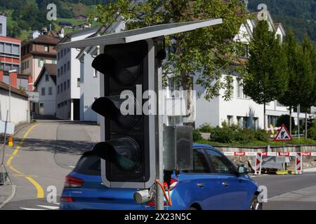 Blaues Auto, das in der Nähe einer tragbaren Ampel vorbeifährt, die von Solarpaneelen auf der Straße betrieben wird, um den Verkehr während der Bauarbeiten in Schwyz zu lenken. Stockfoto