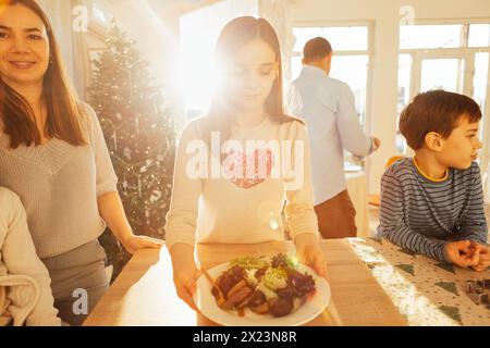 Ein süßer Teenager hält einen Teller mit Kartoffeln und Salat im Speisesaal. Eine glückliche Familie kocht zusammen Weihnachtsgerichte. Kinder und Eltern essen zu Mittag Stockfoto