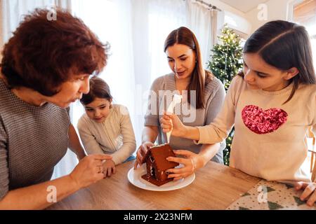 Lächelnde Großmutter mit Tochter und Enkelinnen kochen gemeinsam Weihnachtskekse in der Küche. Reife Frau mit ihren süßen, glücklichen Mädchen schmücken Ginge Stockfoto