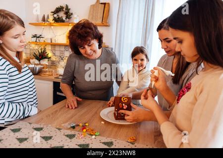 Lächelnde Großmutter mit Tochter und Enkelinnen kochen gemeinsam Weihnachtskekse in der Küche. Reife Frau mit ihren süßen, glücklichen Mädchen schmücken Ginge Stockfoto