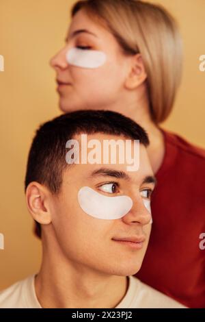 Ein lächelndes Teenagerpaar im Profil mit feuchtigkeitsspendenden Flecken unter den Augen. Ein süßes Mädchen und ein Junge kümmern sich um die Haut des Gesichts. Kosmetisches Verfahren Stockfoto