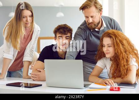 Männlicher Dozent, der auf den Laptop-Bildschirm zeigt und einer Gruppe von Studenten etwas zeigt. Stockfoto