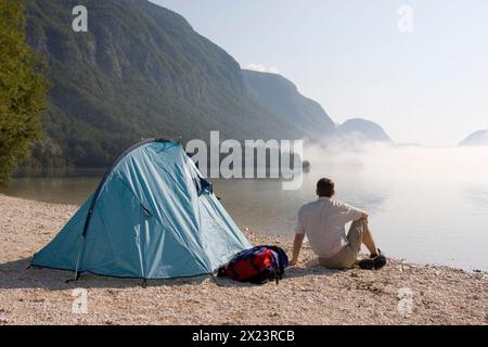 Mann sitzt neben seinem Zelt an einem See im Triglav-Nationalpark in Ukanc, Slowenien Stockfoto