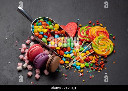 Verschiedene bunte Süßigkeiten, Lutscher und Makronen. Süßigkeiten auf Stein Hintergrund Stockfoto