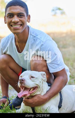 Junger Mann, Porträt und Hund auf dem Rasen mit Glück, spielen mit Pitbull für Tierliebe und Spaß im Freien. Adoption, Pflege und Bindung im Park mit Stockfoto