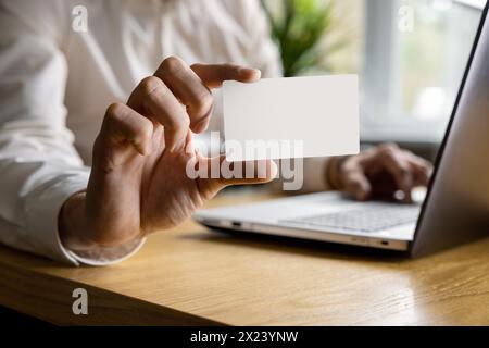 Mann zeigt leere Visitenkarte, während er im Büro am Laptop arbeitet. modell Stockfoto