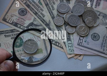 Münze aus russischem Rubel mit Lupe vor dem Hintergrund von Dollars. Zahlungsverzug in Russland und Stärkung des Rubels. Stockfoto