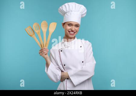 Glücklicher Koch in Uniform, der Holzutensilien auf hellblauem Hintergrund hält Stockfoto