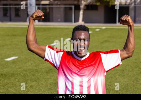 Afroamerikanischer junger männlicher Athlet, der draußen auf dem Feld feiert und die Arme hebt Stockfoto