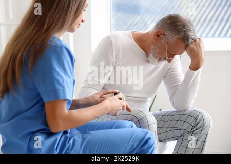 Weibliche Betreuerin, die den Puls von einem älteren Mann im Schlafzimmer nimmt Stockfoto