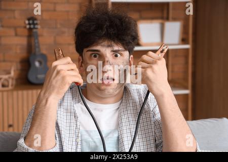 Ein junger Mann mit Verbrennungsgesicht und Überbrückungskabeln zu Hause, Nahaufnahme Stockfoto