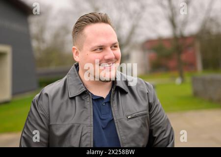 Junger attraktiver Mann in seinen Zwanzigern, der im Frühjahr draußen in einem Park stand und freundlich zu Side aussah Stockfoto